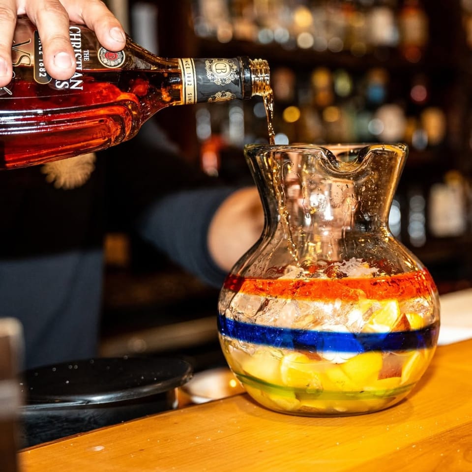 A hand pours liquor from a bottle into a colorful pitcher of sangria at Gaby's Cafe.