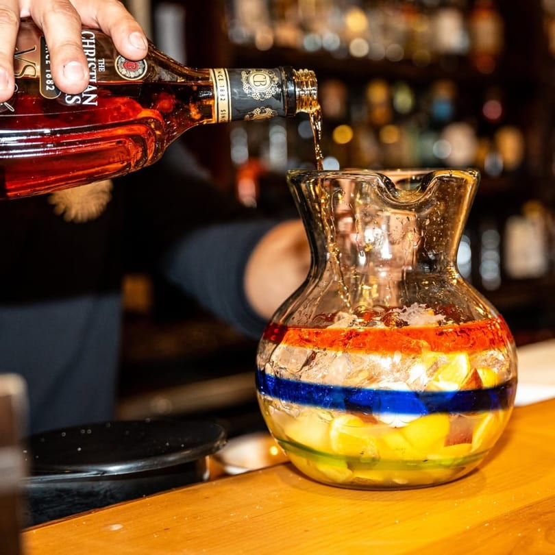 A hand pours liquor from a bottle into a colorful pitcher of sangria at Gaby's Cafe.