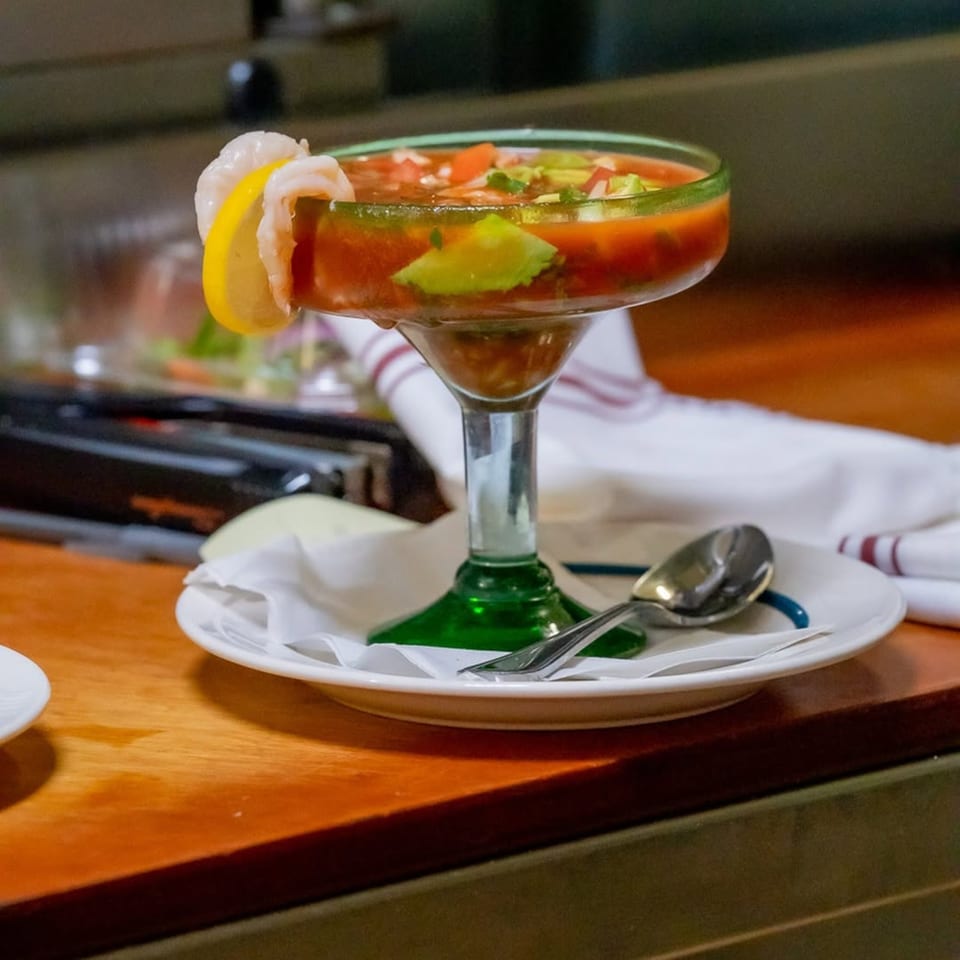 A Mexican shrimp cocktail in a margarita glass with avocado, tomato, and a lemon slice.