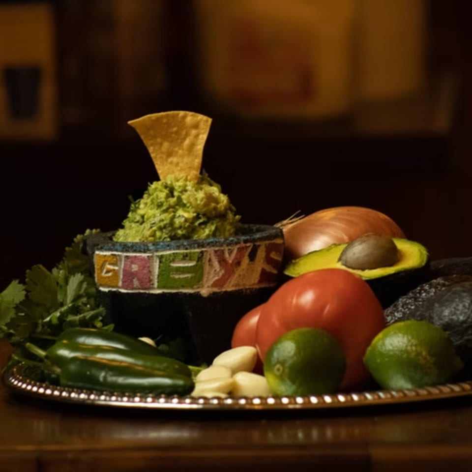 Guacamole with a tortilla chip in a Gaby's Cafe bowl, surrounded by fresh ingredients.