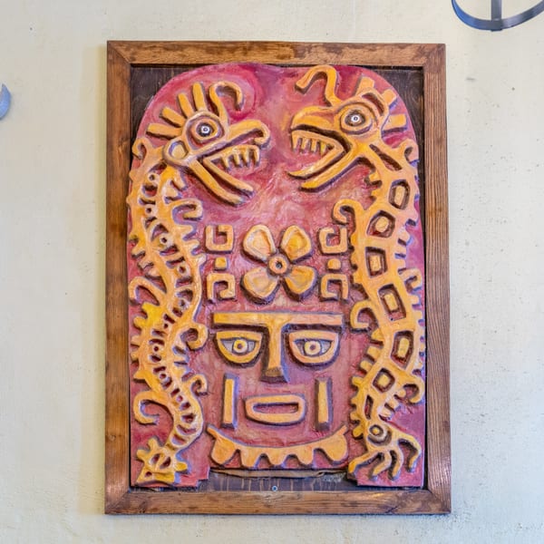 A framed, colorful Mexican-inspired relief carving featuring a face and two dragon-like figures.