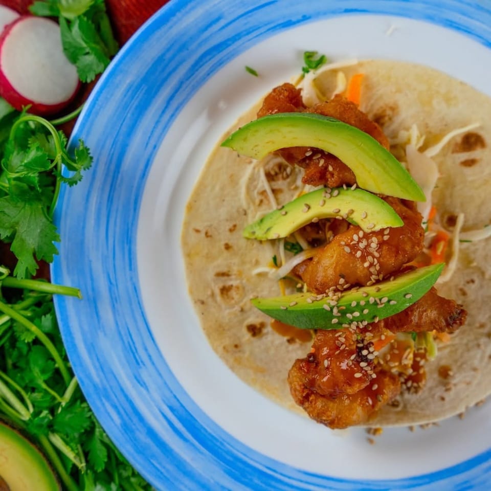 Gaby's Cafe fish taco with avocado slices and sesame seeds on a blue-rimmed plate.